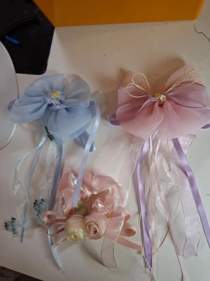 Söta hårrosetter i pastellfärger - Tre håraccessoarer: två stora rosetter i ljusblått och ljusrosa med långa band och dekorativa blommor, samt en scrunchie i ljusrosa med satängrosor. Perfekta för att piffa upp frisyren med en romantisk touch.  35sek/st. 3 for 85 sek.