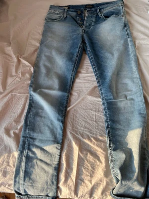  slim fit jeans Jack & Jones - Snygga ljusblå slim fit jeans från Jack & Jones med klassisk femficksmodell och knappgylf. Jeansen har en tvättad look med slitningar och är tillverkade i bomull med lite stretch för extra komfort. Perfekta till en avslappnad stil.