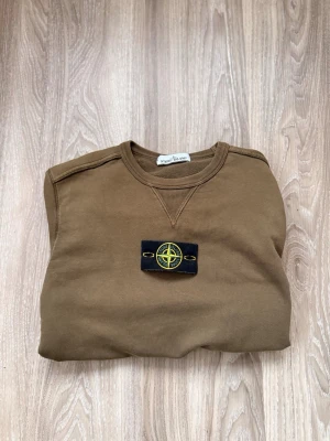  Stone Island - Olivgrön sweatshirt från Stone Island med klassisk rund halsringning och ribbade muddar. Tröjan har den ikoniska Stone Island-loggan på vänster ärm och är tillverkad i mjuk bomull. OBS fins ett litet hån på höger armen men är man en kunnig person så går det att laga hur änkelt som helst! Om du ser att den är lite fläckig så är det ljuset och vi kommer rengöra plagget ordentligt innan vi postar! Också vicktigt att säga att tröjan är 100% ÄKTA. Passar mellan 168-175cm