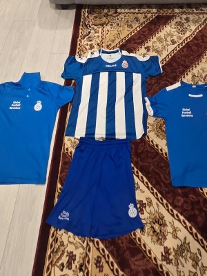 Espanyol Barcelona fotbollskläder set - Säljer ett set med Espanyol Barcelona fotbollskläder från Kelme. Inkluderar en blåvit randig matchtröja, två blå träningströjor med tryck och ett par blå shorts. Alla plagg har klubbens logga och texten 'Global Football Barcelona'. Perfekt för träning eller match.