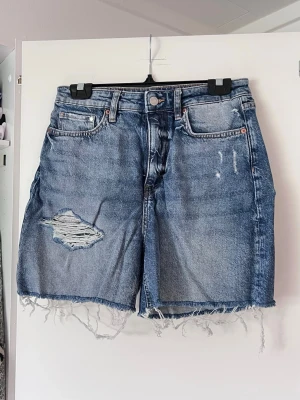 Blå denimshorts med slitningar från H&M - Säljer ett par blå denimshorts med och slitningar. Knapp och dragkedja framtill. Storlek 38, mycket bra skick! Perfekta för vår och sommar <3