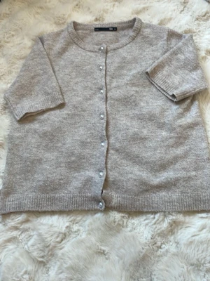 Beige kofta med pärlknappar 157 - Mysig beige kofta från 157 med pärlknappar framtill. Koftan har rund halsringning, halvlånga ärmar och ribbade muddar. Perfekt att slänga över en topp för en chill look. Materialet känns mjukt och skönt mot huden. Stolen xs, pris 20kr