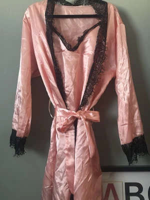 Morgonrock & linne - Snygg rosa morgonrock i glansigt satinmaterial med svarta spetsdetaljer längs kanterna och ärmsluten. Knytskärp i midjan och matchande spetskantad topp medföljer. Perfekt för en lyxig och avslappnad känsla hemma. Inget fel på kläderna, bara blivit skrynkligt i garderoben 💕(för jag har för mycket kläder så nu rensas det) 