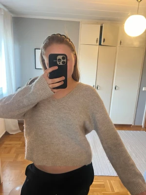 Beige stickad tröja med v-ringning - Mysig beige stickad tröja med v-ringad hals och avslappnad passform. Tröjan har långa ärmar och ribbade muddar vid ärmslut och nederkant. Perfekt för lager på lager och enkel att matcha till olika outfits.