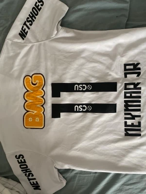  Neymar Jr santos t shirt nike - Säljer en vit Santos matchtröja från Nike med Neymar Jr och nummer 11 på ryggen. Tröjan har flera sponsorloggor, bland annat BMG och Netshoes, samt Santos klubbmärke på bröstet. Tillverkad i lätt och ventilerande material, perfekt för fotboll.