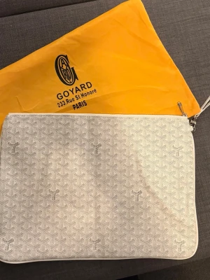Vitt datorfodral  - Snyggt vitt datorfodral med ett klassiskt mönster och subtila loggor över hela väskan. Tillverkad i tåligt material med dragkedja upptill. Perfekt för att bära det viktigaste och ger en clean look.