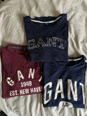 GANT t-shirt med tryck - Säljer 3st Gant T-shirts. De blåa tröjorna är i strl S och den vinröda är i strl 158/164 men skulle säga att den är som en strl S.  Något spruckna i trycket och den ena blåa t-shirten är missfärgad i trycket. Svårt att få med på bild
