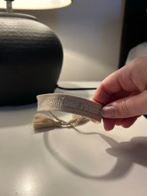Äkta Dior armband - Äkta original armband från Dior & broderi i vitt. Armbandet har justerbar knytning med tofsar i ändarna. Mycket fint skick. Ser ny ut. Original pris 4000kr