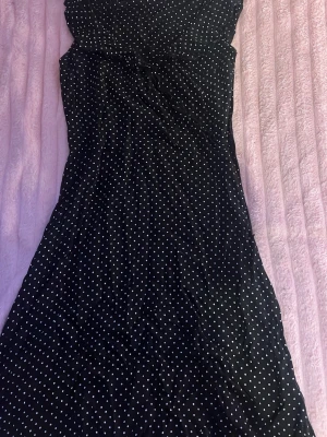 Svart prickig klänning med dragkedja - Svart klänning med vita prickar och smickrande passform. Klänningen har en dragkedja i sidan och är i en lätt, luftig kvalitet. Perfekt för dig som gillar klassiska mönster och enkel stil.