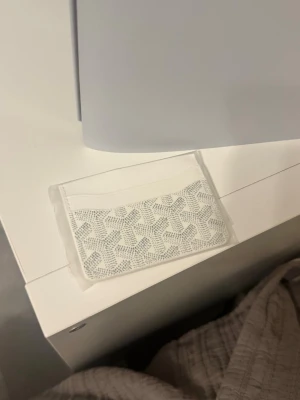 Vit kortfodral med spetsmönster - Säljer ett stilrent vitt kortfodral med transparent framsida och ett snyggt spetsmönster i vitt. Perfekt för att förvara kort på ett smidigt och trendigt sätt. Enkel och tunn design som får plats i fickan eller väskan. Med box 