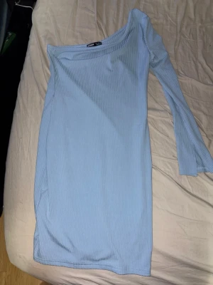 Ljusblå one shoulder klänning SHEIN - Trendig ljusblå ribbad klänning från SHEIN i one shoulder-modell med lång ärm på ena sidan. Klänningen är kort och har en slim passform som framhäver figuren. Perfekt för dig som gillar stilrena och moderna plagg.Storlek S / EU 36