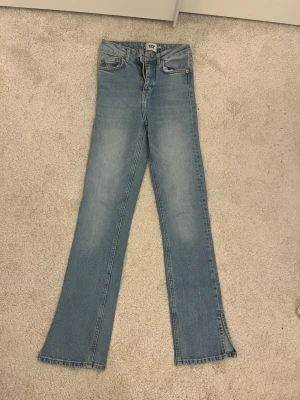 Ljusblå bootcut jeans med slits - Säljer ett par ljusblå bootcut jeans med slits nertill på benen. Jeansen har klassisk femficksdesign, normal midja och är tillverkade i denim. Perfekta för en avslappnad och trendig look.