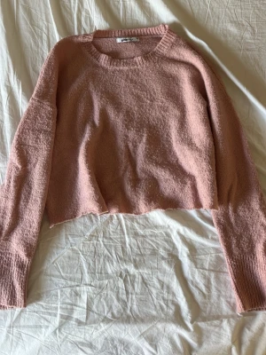 Rosa stickad cropped tröja Gina Tricot - Säljer en rosa stickad cropped tröja från Gina Tricot. Tröjan har rund halsringning, långa ärmar och ribbstickade muddar. Materialet är mjukt och fluffigt, perfekt för att skapa en avslappnad look.