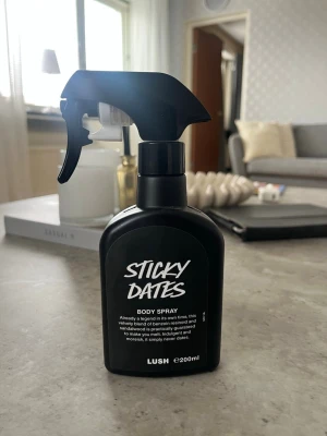 Lush Sticky Dates Body Spray 200ml - Sticky Dates Body Spray från Lush i en svart sprayflaska på 200 ml. Doften är söt och varm med inslag av dadlar och sandelträ. Flaskan har en modern, matt finish och tydlig vit text på framsidan. Perfekt för dig som gillar unika och djupa dofter. OBS! Hälften kvar i flaskan!!!