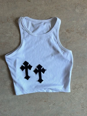  ribbad ”chrome hearts” linne  - Säljer en vit ribbad croppad linnetopp med två svarta kors framtill.  Sitter tight och passar XS-S, den är mjuk och stretchig. Den slutar typ vid naveln så inte direkt croptop.