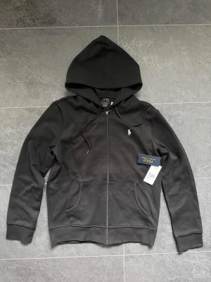 Svart hoodie från Polo Ralph Lauren - Hej säljer en svart ralp lauren zip som är helt ny och just använd 1 gång då den inte kommer till nån användning alls! Riktigt fint klassiskt zip 