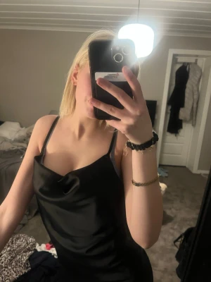 Svart satin topp med smala band - Snygg svart topp i satin med tunna axelband och lätt draperad urringning. Toppen har en figurnära passform och är perfekt för dig som gillar en stilren och elegant look.