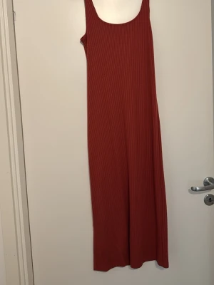 Rostbrun ribbad långklänning - Säljer en enkel och snygg rostbrun långklänning med ribbad struktur. Klänningen är ärmlös och har en rundad urringning. Perfekt för dig som gillar minimalistisk stil och vill ha något bekvämt och trendigt.
