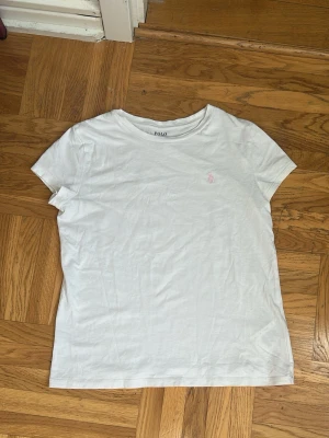 Vit t-shirt från Polo Ralph Lauren - Säljer en vit t-shirt från Polo Ralph Lauren med diskret rosa logga broderad på bröstet💕💕 T-shirten har rund halsringning och korta ärmar💕💕I mycket bra skick💕💕Jag säljer den för 100 kr💕💕Hör av er vid intresse💕💕