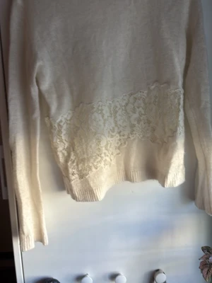 Vit stickad tröja med spetsdetalj från Zara - Säljer en krämvit stickad tröja med lång ärm och bred spetsdetalj över magen. Tröjan har ribbstickade muddar vid ärmslut och nederkant. 