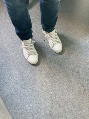 Vita sneakers från Axel Arigato - Stilrena vita sneakers från Axel Arigato med klassisk låg profil och vita snören. Skorna är tillverkade i slätt läder och har diskret logga på sidan. Perfekta för en clean och modern look. Passar till allt! Ordinarie pris 2000kr