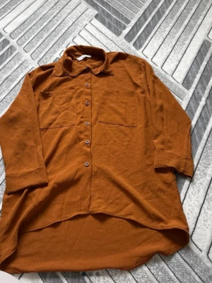 Brun oversized skjorta i linne - Snygg oversized skjorta i brun färg med långa ärmar och två bröstfickor. Skjortan har knappar framtill och är tillverkad i ett luftigt linnematerial, perfekt för en avslappnad stil.