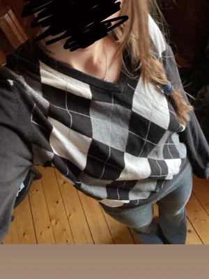 Argyle mönstrad tröja i svart och grått - Snygg långärmad tröja med klassiskt argyle-mönster i svart, grått och vitt. Tröjan har V-ringning och ribbade muddar vid ärmslut och nederkant. Egentligen herr eller unisex storlek tror jag, men jag har andvänt den som tjej med storlek 36/S och det har funkat jättebra. Tror även den hade passat någon med storlek 38 eller M bra.