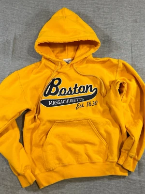 Boston Massachusetts Spell Out Hoodie Yellow Small - Boston Massachusetts hoodie in bright yellow with big spell-out chest logo. Clean collegiate / USA vibe. Soft fleece inside, kangaroo pocket, classic pullover fit.  Size S  Measurements (cm): P2P 50, S2S 50, Length 60, Sleeve 54, Waist 42  Good used condition, normal wear.  Unisex fit. 
