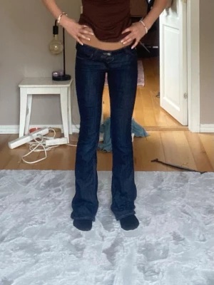 Mörkblå bootcut jeans low waist - Snygga mörkblå bootcut jeans med låg midja och klassiska fem fickor. Jeansen har en tight passform upptill och släpper ut vid benen för en trendig siluett. Perfekta till sneakers eller boots för en cool vardagslook.