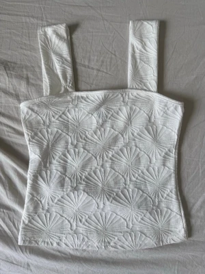 Vit broderad linnetopp - Säljer en vit linnetopp med breda axelband och broderat mönster över hela toppen. Toppen har en figurnära passform och är perfekt för sommardagar. Materialet känns svalt och bekvämt.