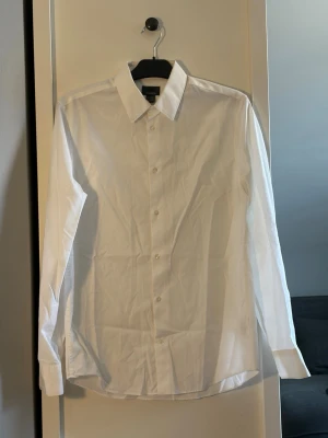 Vit klassisk skjorta från HM - Säljer en stilren vit skjorta från HM premium cotton med klassisk krage och knäppning framtill. Skjortan har lång ärm och är tillverkad i bomull, perfekt för en clean och tidlös look.