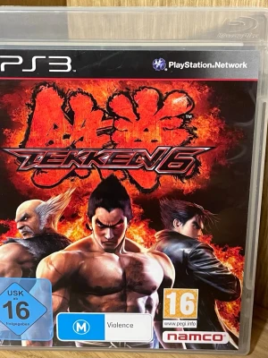 Tekken 6 till PS3 - Tekken 6 till PlayStation 3 är ett klassiskt fightingspel med intensiv action och ikoniska karaktärer. Omslaget har en eldig bakgrund med tre kända figurer från spelet. Spelet levereras i ett plastfodral med färgstark grafik och tydlig logotyp.
