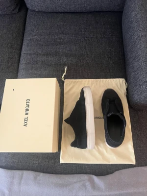 Laceless Axel Arigatos 360 - Stilrena svarta sneakers från Axel Arigato med ovandel i mocka och vit gummisula. Klassisk låg modell med minimalistisk design och diskreta detaljer. Perfekta för dig som gillar en clean och modern look.