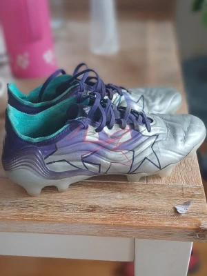 Adidas Copa silvriga fotbollsskor - Snygga Adidas Copa fotbollsskor i silver med lila och turkosa detaljer samt svarta och röda grafiska mönster. Skorna har snörning och en låg profil, perfekt för spel på gräs. Champions league copa skor, 40 2/3, vid högern har lite slitage vid längst fram. Skorna är elite. Skorna är till för fg.