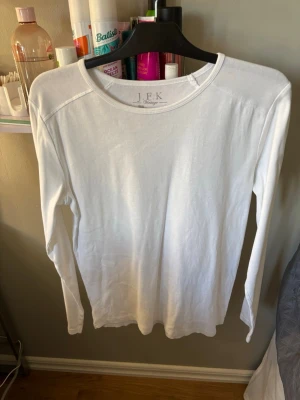 Vit långärmad topp från J.F.K Vintage - En stilren vit långärmad topp från J.F.K Vintage. Tillverkad i mjuk bomull med rund halsringning och enkel design som passar till många olika outfits. Perfekt basplagg för garderoben.