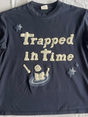 Mörkblå T-shirt Trapped in Time - Cool mörkblå T-shirt med trycket 'Trapped in Time' och ett skelettmotiv på framsidan. Broderad text 'BROKEN' på ärmen. Skön passform och rund halsringning, perfekt för en avslappnad stil.
