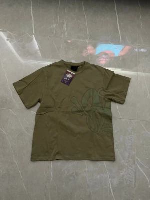 Olivgrön t-shirt med tryck - Snygg olivgrön t-shirt från SYNA WORLD med ett stort, diskret tryck i liknande ton på både fram- och baksidan. Klassisk passform med rund hals och korta ärmar. Perfekt för en avslappnad streetwear-look.