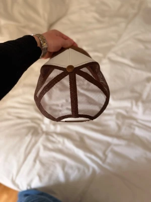 Brun och vit keps från Bvaldi - Snygg keps från bvaldi med vit frontpanel, brunt mesh-tyg baktill och brunt böjt skärm. Kepsen har broderad logga framtill och justerbar snapback. Endast testat!! 