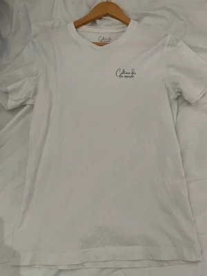 Vit t-shirt Culture de la mode - Vit t-shirt från Culture de la mode med tryck på bröstet och ett större tryck på ryggen i form av en meny. Klassisk passform med rund hals och korta ärmar. Tillverkad i mjuk bomull, perfekt för en avslappnad stil.