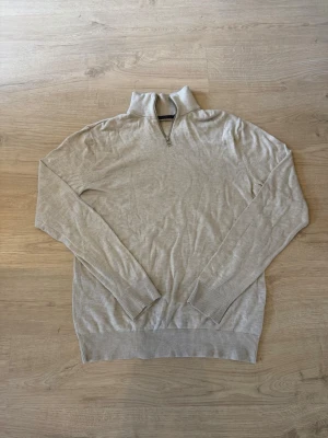 Beige halvzip tröja i tunn stickning - Snygg beige tröja med halv dragkedja och hög krage. Tunn stickning och långa ärmar med ribbade muddar och nederkant. Perfekt för lager-på-lager och enkel att matcha med olika outfits.