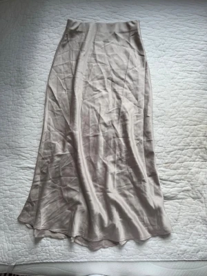 Beige långkjol i satin - Säljer en beige långkjol i glansigt satinliknande material. Inga fler bilder då de ligger i flyttlåda.