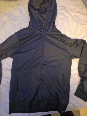 Svart EA7 hoodie - Snygg svart EA7 hoodie med hel dragkedja framtill och två fickor. Modellen har huva med dragsko och ribbade muddar vid ärmslut och nederkant. Perfekt för en avslappnad och sportig stil.