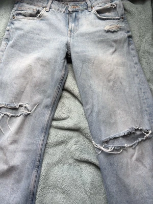 Ljusblå slitna jeans med hål - Säljer ett par ljusblå jeans med flera slitningar och stora hål på benen. Jeansen har klassisk femficksmodell och raka ben. Materialet är denim i bomull och de har en avslappnad, trendig look.