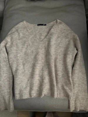 Beige stickad tröja med V-ringning - Mysig beige stickad tröja från lager 157 med V-ringad hals och långa ärmar. Tröjan har en avslappnad passform och ribbade muddar vid ärmslut och nederkant. Perfekt för lager på lager och enkel att matcha med olika stilar. pris kan diskuteras 