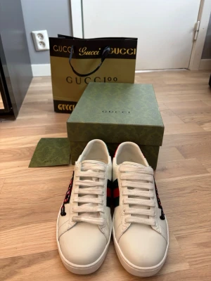  Ace sneakers med orm - Säljer ett par vita  Ace sneakers i läder med den ikoniska gröna och röda webbranden på sidan och en broderad röd orm. Skorna har vita snören och klassisk låg siluett. Perfekta för dig som vill sticka ut med lyxig streetstyle. Pris kan diskuteras 