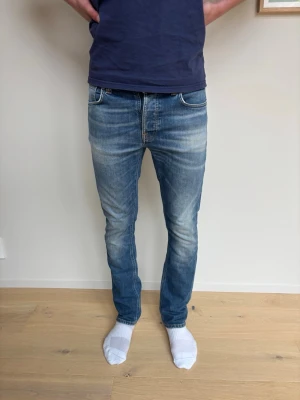 Blå slim fit jeans från Nudie - Snygga blå slim fit jeans från Nudie. Jeansen har orangea sömmar på bakfickorna. Perfekta för en avslappnad och trendig stil.