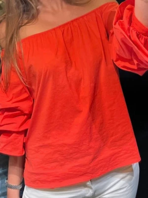 Röd offshoulder blus med vida ärmar - Trendig röd offshoulder blus med vida, rynkade ärmar. Toppen har en avslappnad passform och är tillverkad i mjuk bomull som känns skön mot huden. Perfekt att styla med både jeans och kjol för en cool look.
