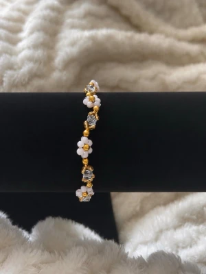 Guldfärgat armband med blommor - Gullig armband med små vita pärlblommor, guldfärgade pärlor och transparenta kristall pärlor. 