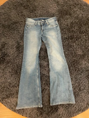Blå bootcut jeans med ljus tvätt - Snygga blå bootcut jeans med ljus tvätt och klassisk femficksdesign. Jeansen har utsvängda ben och låg midja, perfekta för en avslappnad och trendig look. Tillverkade i denim med lätt slitning framtill och bak.