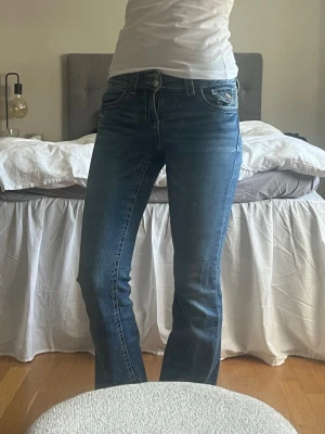 Blå bootcut jeans  - Snygga blå bootcut jeans från Gina tricot med ljusa slitningar. Jeansen har låg midja, markerade sömmar och en liten myntficka med knappdetalj. Perfekta för dig som gillar en avslappnad men trendig look.